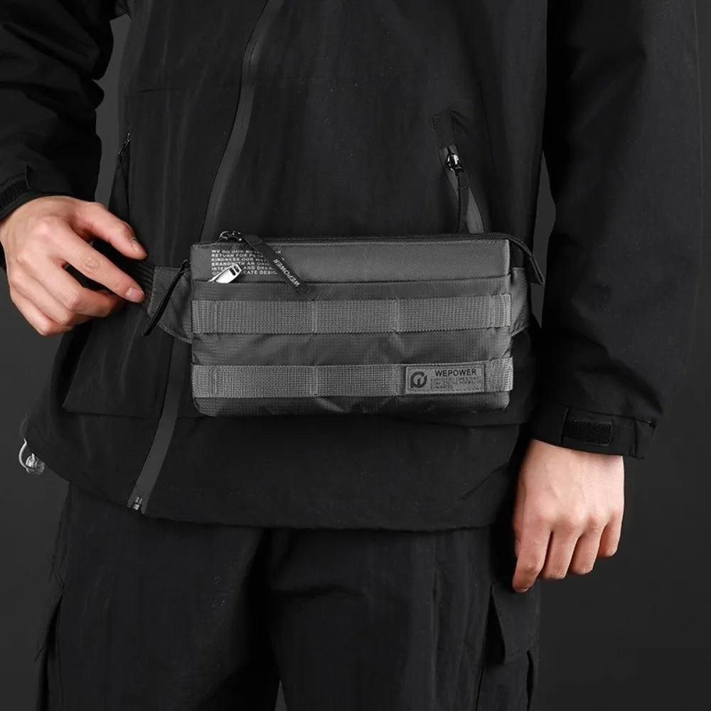 A person wearing a black jacket holds a black versatile fashion chest bag with a strap.