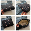 A black embroidered makeup pouch with a zipper is shown being held against a denim jacket.