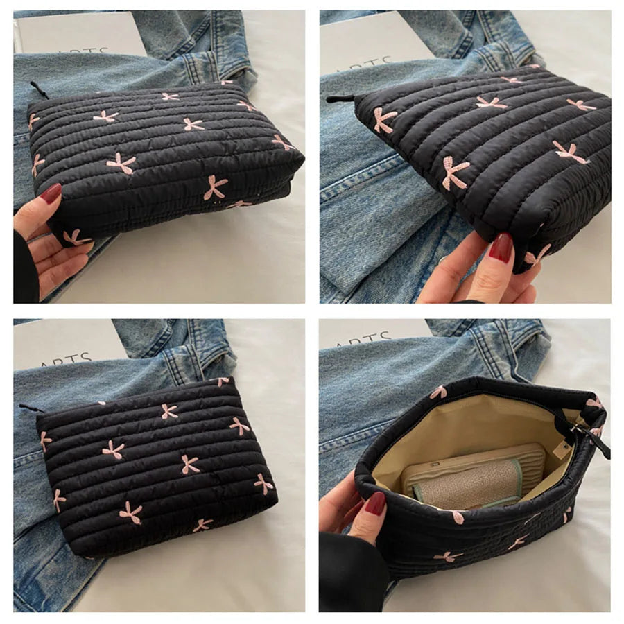 A black embroidered makeup pouch with a zipper is shown being held against a denim jacket.