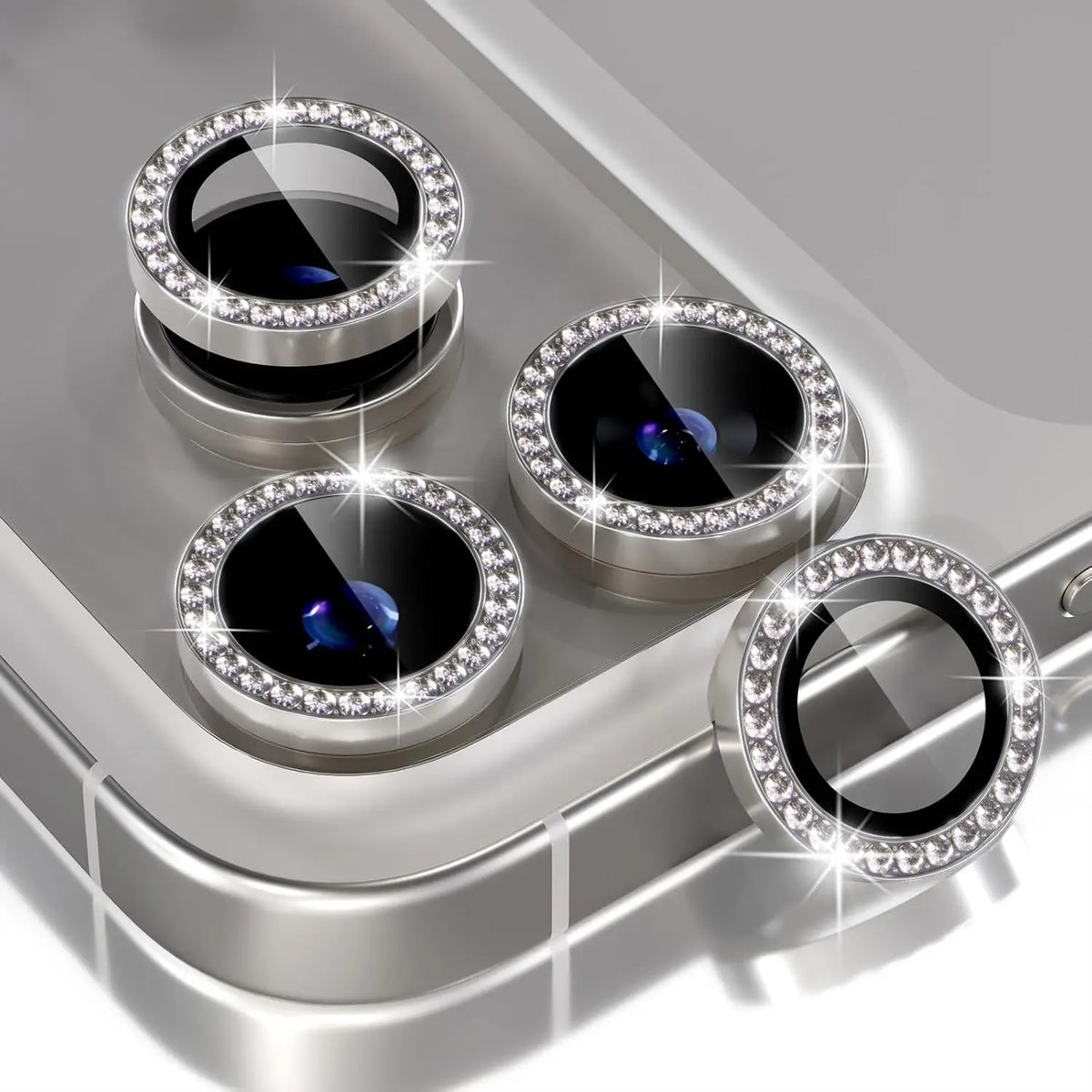 A silver camera lens protector with a glitter diamond lens and metal frame resting on a gray surface.