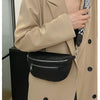 A woman wearing a beige trench coat holds a black PU leather multi-pocket crossbody bag.