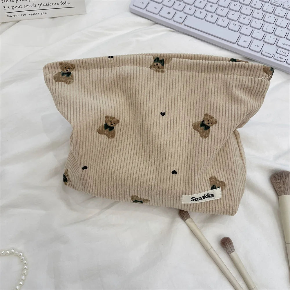 A beige corduroy clutch bag featuring small brown bear embroidery, shown on a white surface.