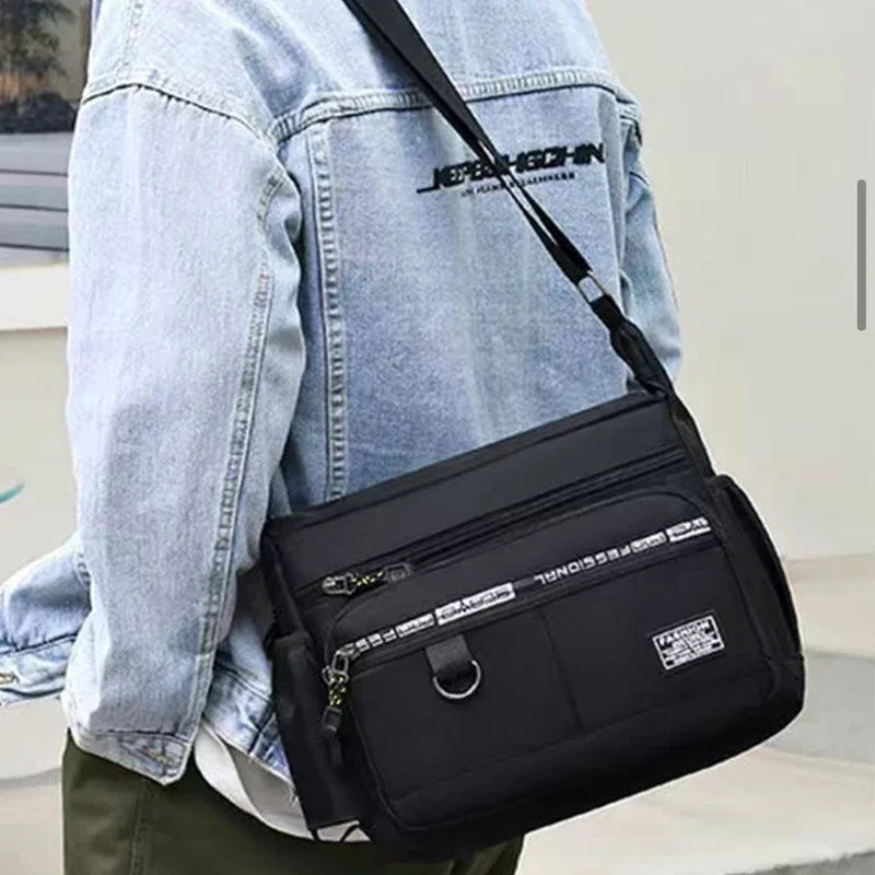 A black men's business crossbody bag is shown against a light blue denim shirt.