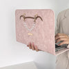 A pink PU laptop sleeve with gold hardware and a clear chain detail is shown being held by a person.