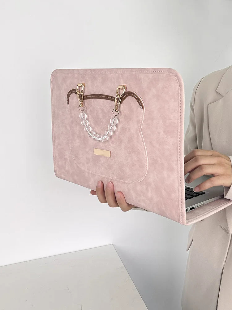 A pink PU laptop sleeve with gold hardware and a clear chain detail is shown being held by a person.