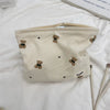 A beige corduroy clutch bag with a light yellow ribbed texture and small brown bear embroidery.