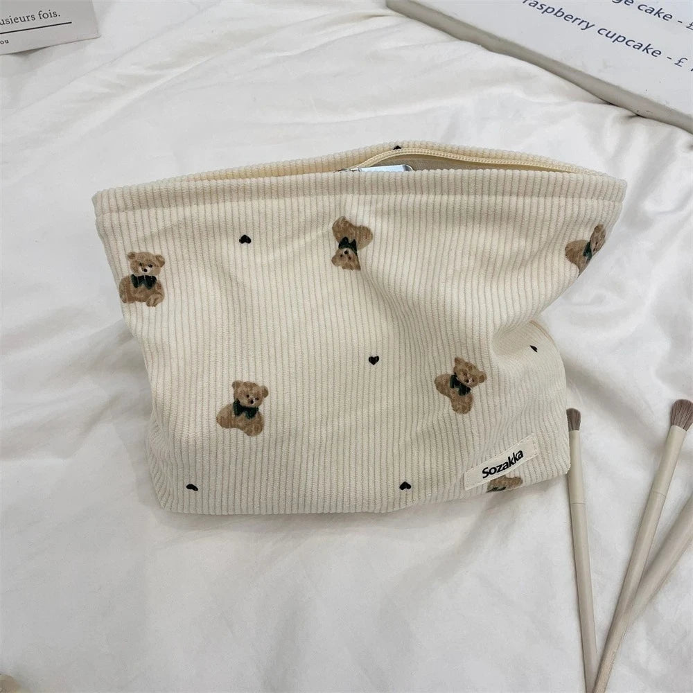 A beige corduroy clutch bag with a light yellow ribbed texture and small brown bear embroidery.