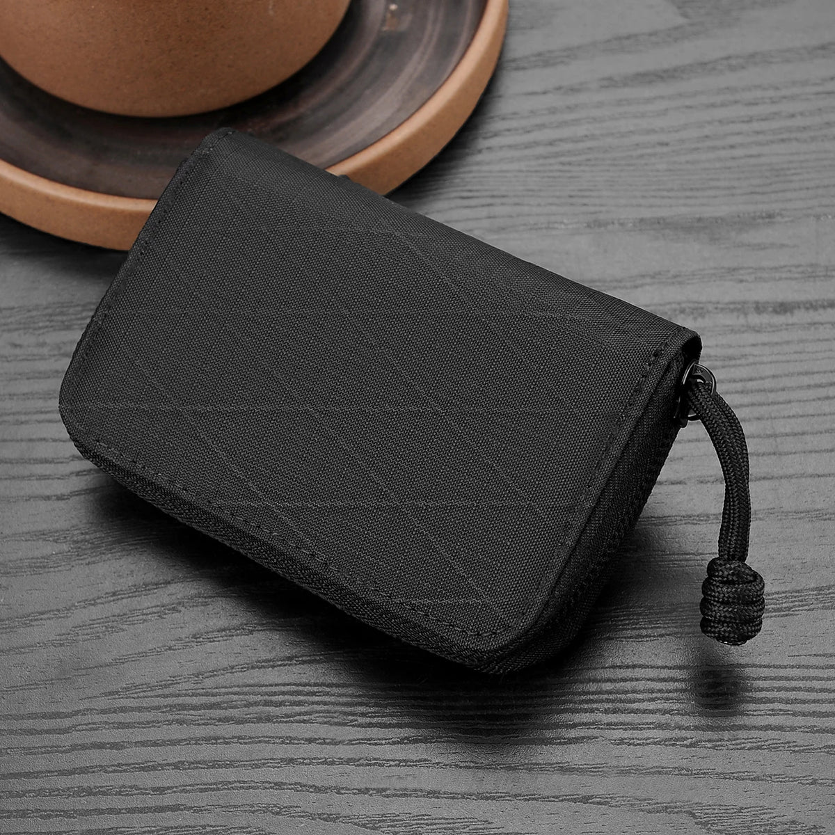 A black RFID zipper wallet lying on a gray wooden surface next to a brown ceramic cup.