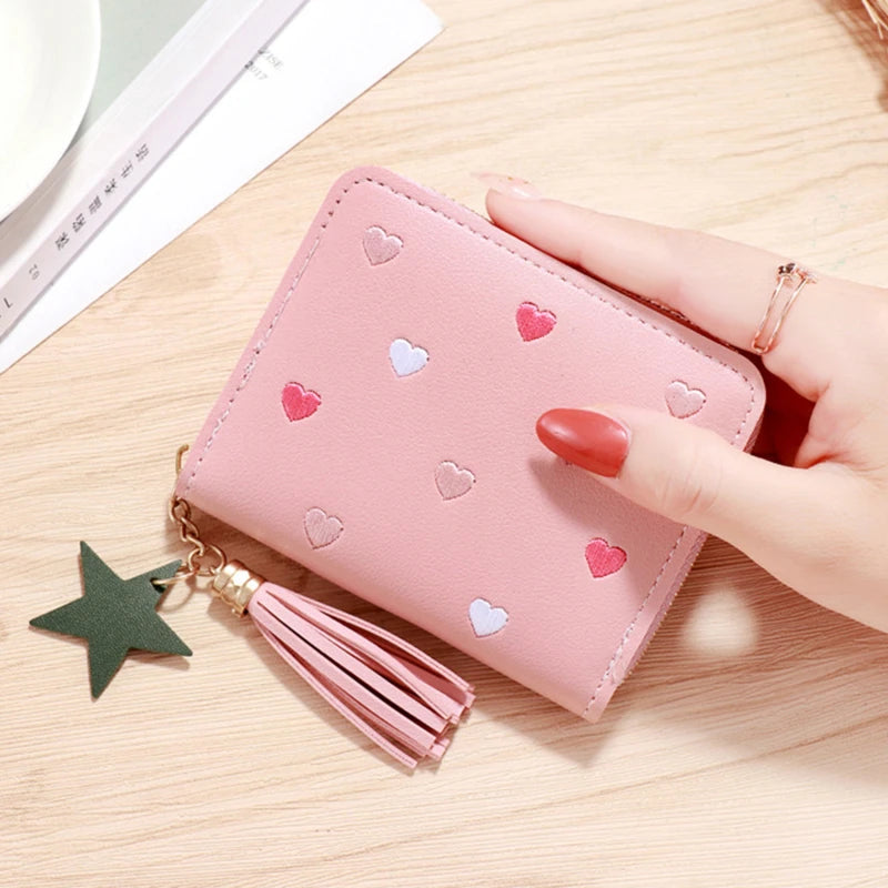 A pink PU leather wallet with a zipper closure and a green star tassel resting on a wooden surface.