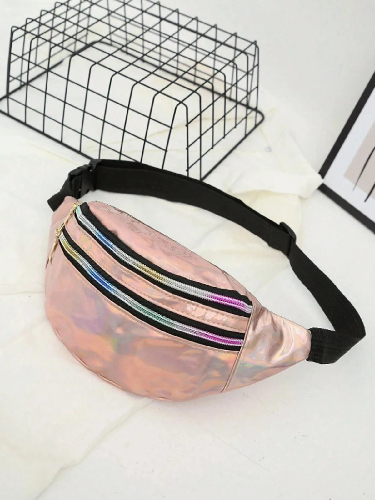 A pink holographic sequin waist bag with a black adjustable strap is displayed on a white surface.