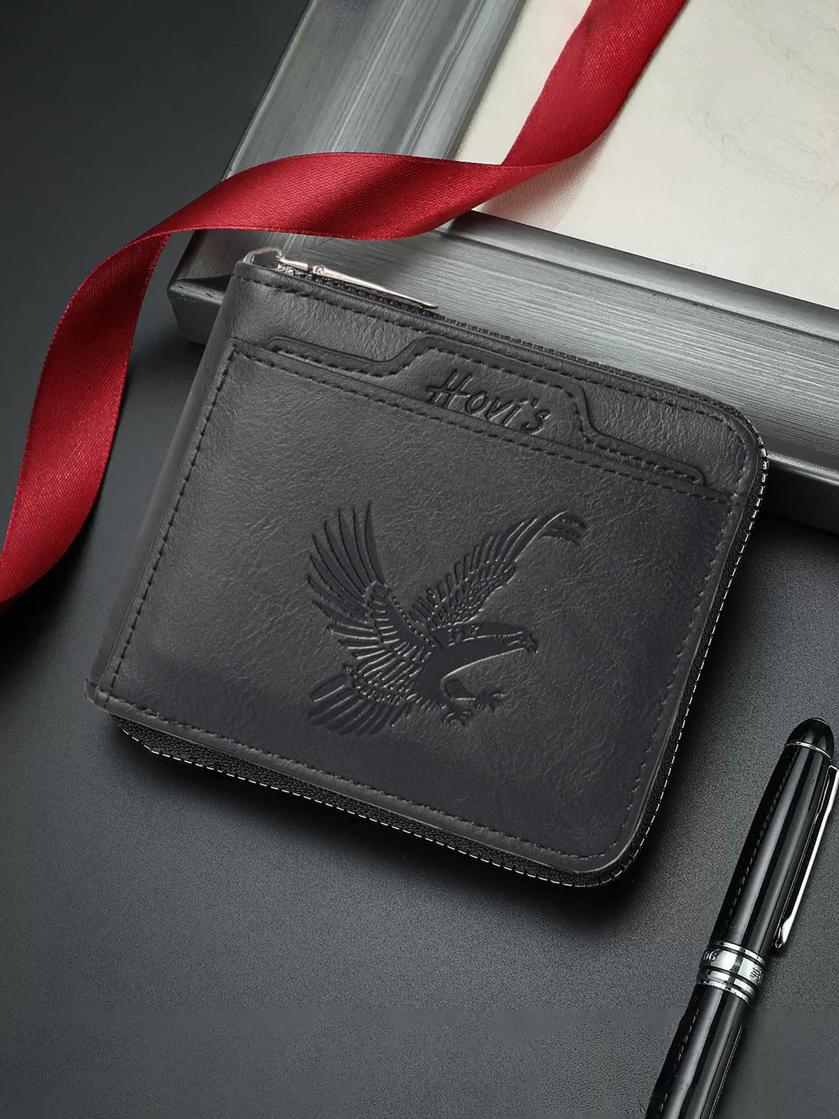 A dark gray embossed PU leather slim wallet with a silver zipper and a red ribbon lying next to it.