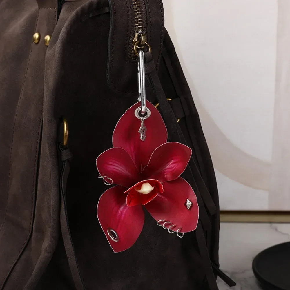 A realistic deep red orchid flower keychain hanging from a zipper pull on a dark brown backpack.