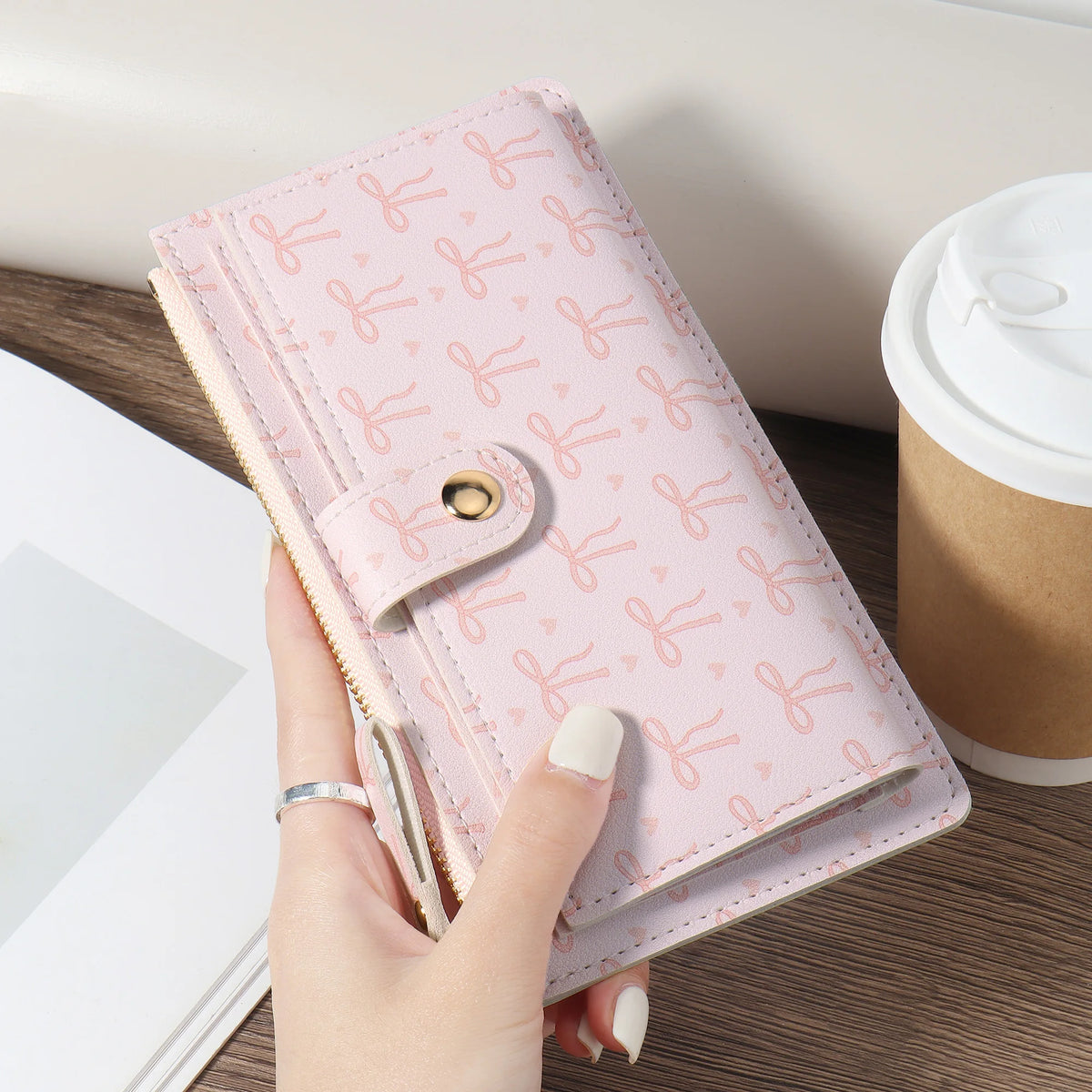 A pink folding multi-card wallet with a floral pattern is held by a hand on a wooden surface.