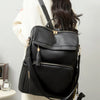 A woman is holding a black vintage tassel backpack with gold hardware against a light gray background.