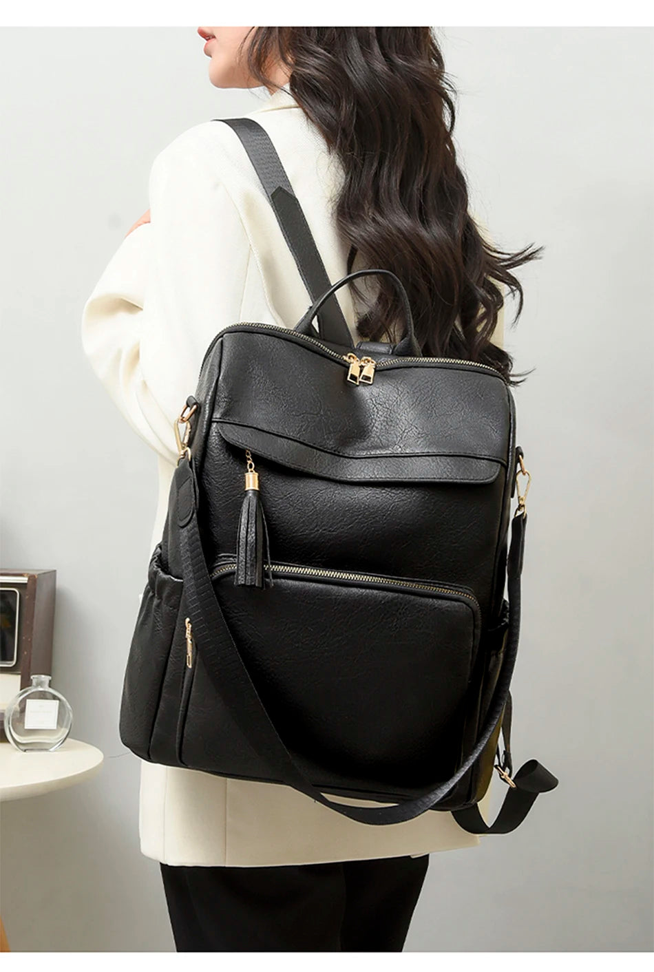 A woman is holding a black vintage tassel backpack with gold hardware against a light gray background.