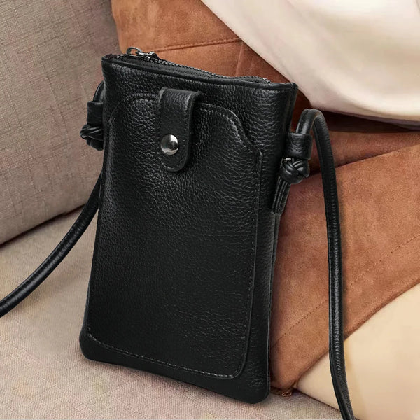 A black PU leather crossbody bag with a zipper and strap resting on a beige fabric surface.