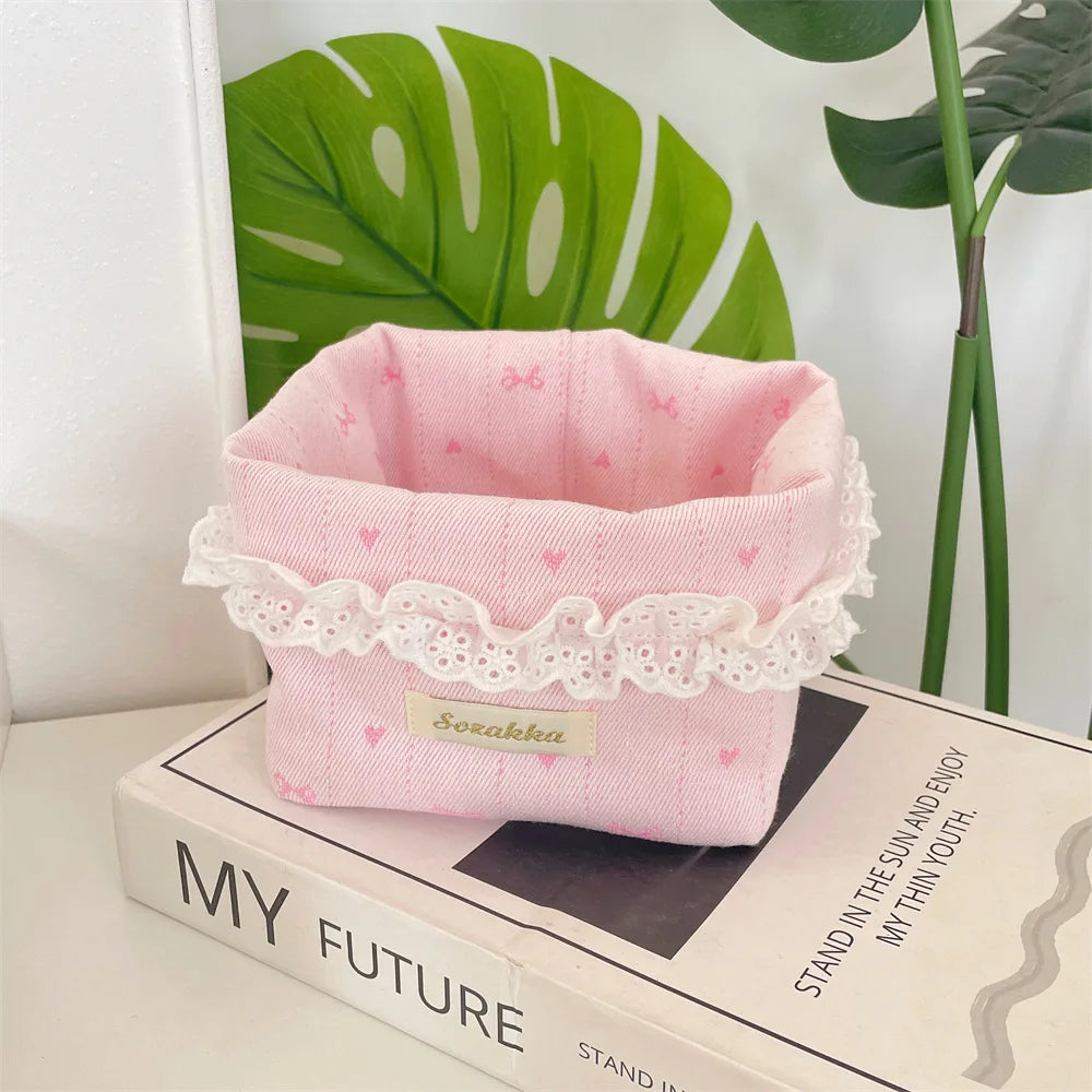Light pink fabric storage basket with a delicate lace trim and heart details resting on a book.