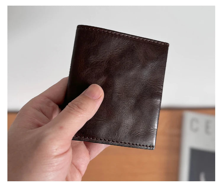 A hand holds a dark brown genuine leather bifold wallet for men.