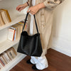 A woman holds a black woven bucket shoulder bag while standing next to a shelf of books.
