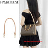 A woman is holding a brown leather bag with gold hardware and a matching strap against a white background.