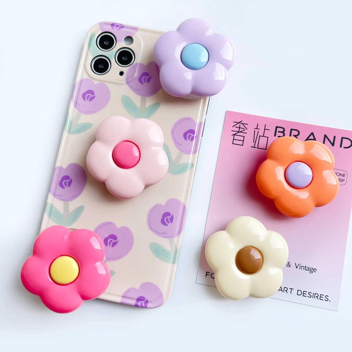 A pink and purple phone case features floral designs, accompanied by three colorful flower rings.