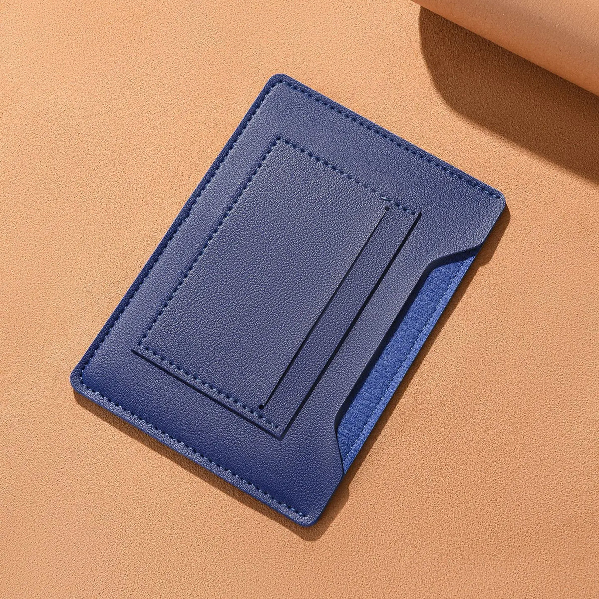 Portefeuille de voyage fin bleu foncé plié et posé sur un fond orange clair.