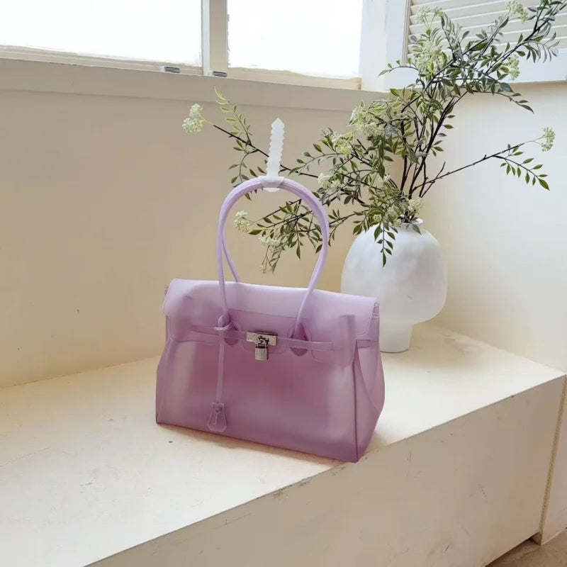 Lavendel-Sommer-Jelly-Schultertasche mit weißem Quaste neben einer Vase mit grünem Laub