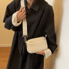 A woman wearing a black coat holds a cream vegan PU crossbody bag with a patterned strap.
