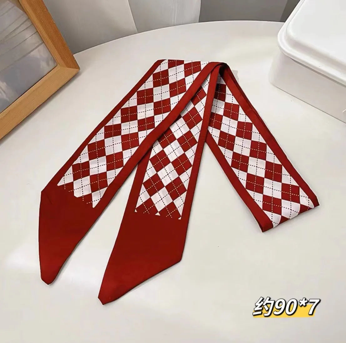 Écharpe de soie à carreaux rouges et blancs pliée sur une surface blanche.
