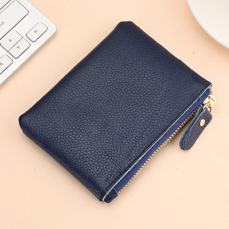 A dark navy genuine leather mini zipper coin and card purse resting on a light beige surface next to a white computer keyboar