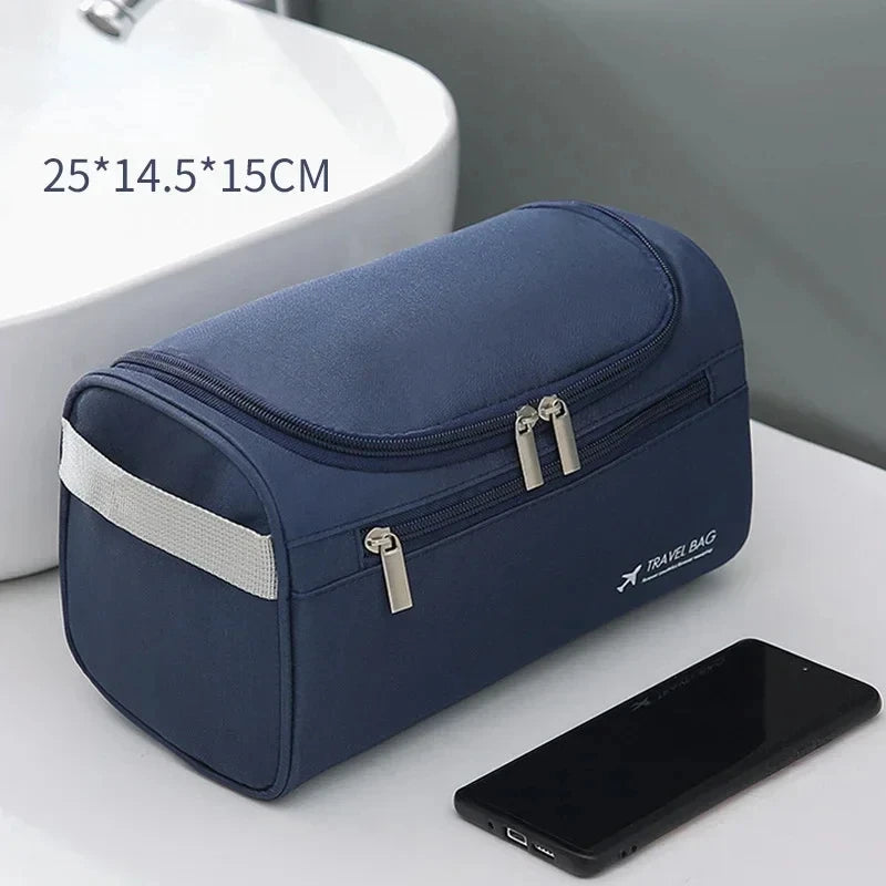 A navy blue durable hanging leather toiletry bag next to a smartphone and a white sink.