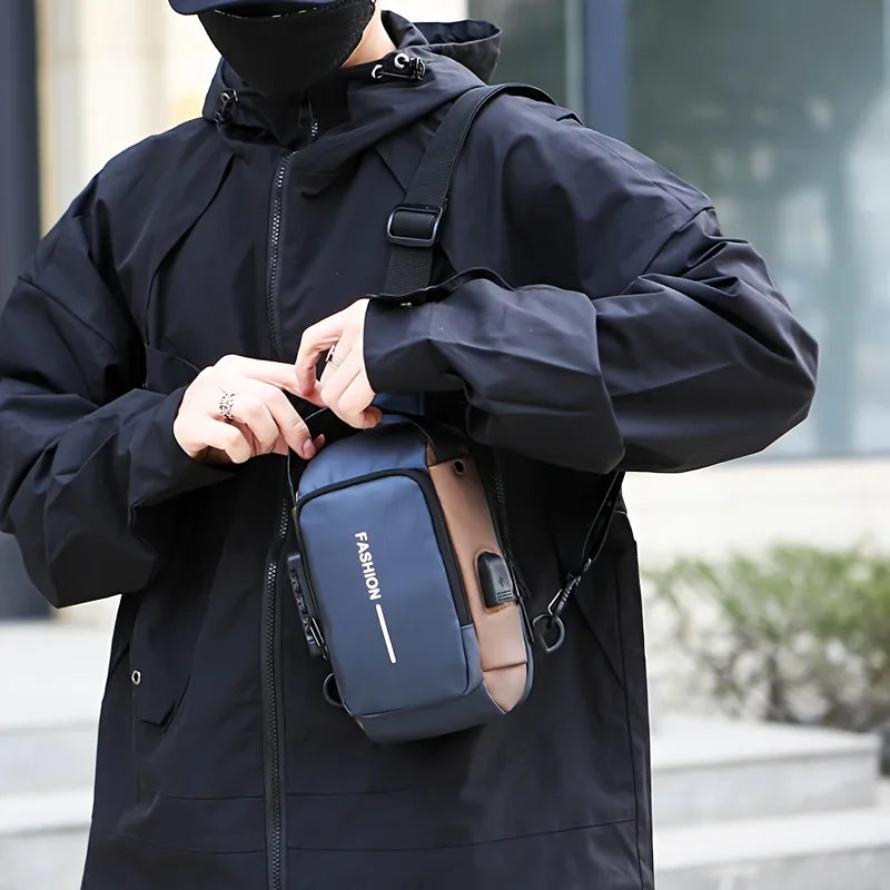 A person wearing a black raincoat is holding a navy blue and tan Oxford sling bag for commuting.