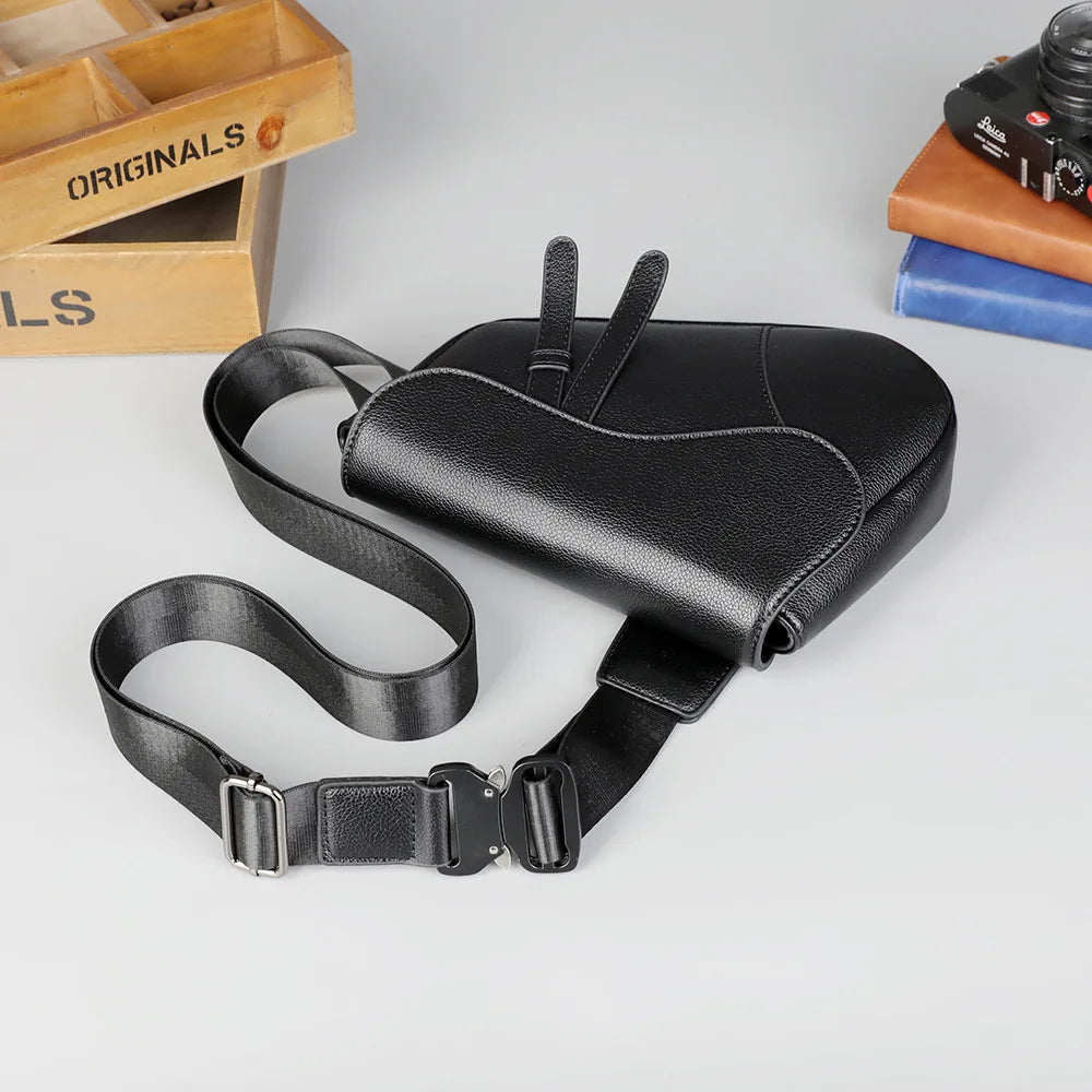 Black men's solid color chest bag with a black strap lying on a light gray surface.