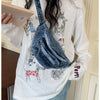 Une femme tient un sac bandoulière en denim délavé vintage contre un chemisier à manches longues blanc.