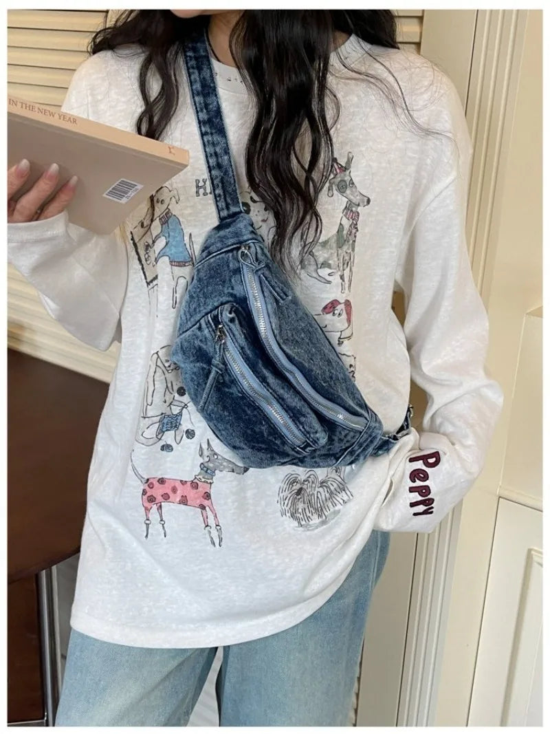 Une femme tient un sac bandoulière en denim délavé vintage contre un chemisier à manches longues blanc.