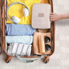 Braune Roll-Organizer-Schale gefüllt mit gelbem Shirt, blauen Jeans und einer Beigetasche mit Toilettenartikeln.