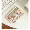 A beige leather card wallet with a floral pattern rests on a white desk next to a laptop keyboard.