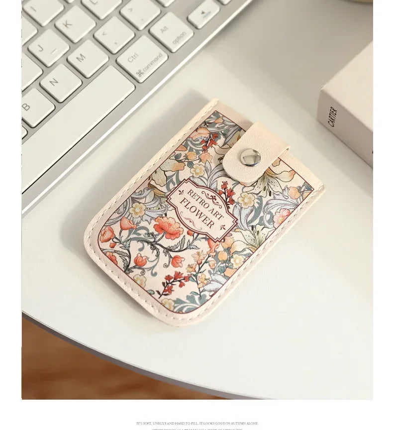 A beige leather card wallet with a floral pattern rests on a white desk next to a laptop keyboard.