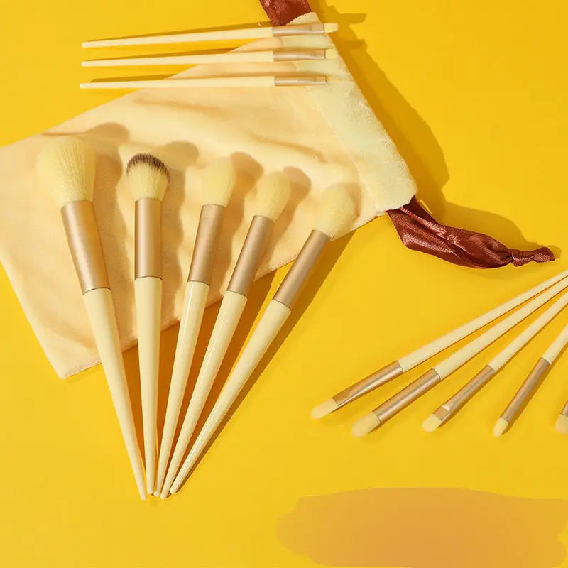 Una colección de 13 brochas de maquillaje profesionales en varios tonos y tamaños sobre un fondo amarillo.