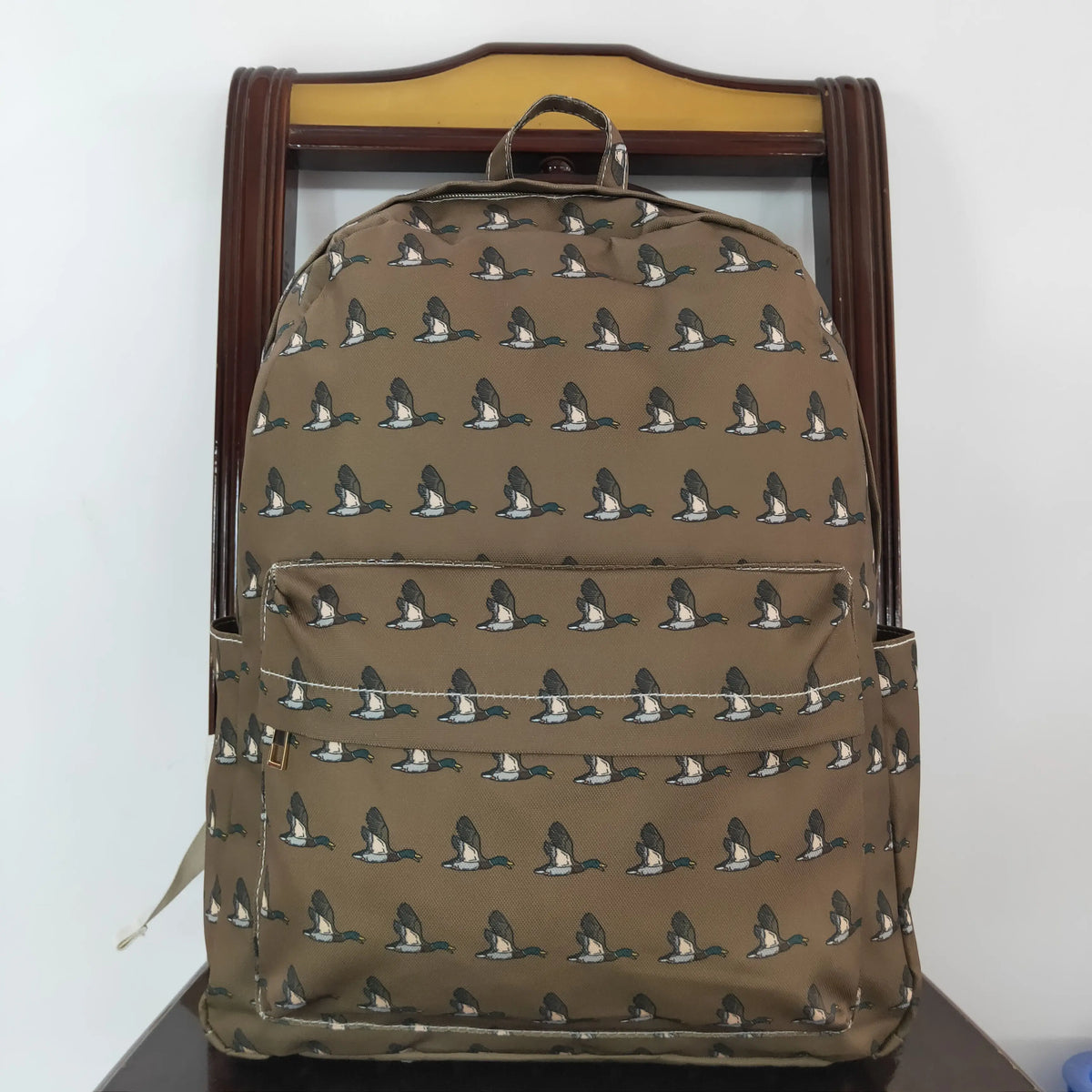 A brown camouflage backpack featuring small animal print patterns, displayed on a wooden hanger.