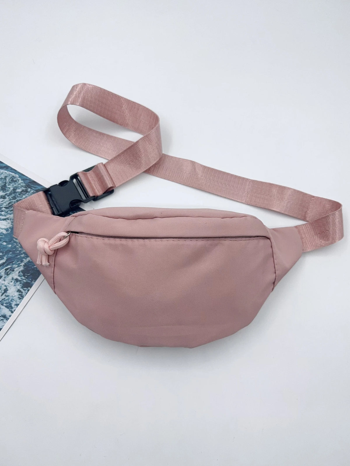 Sac bandoulière en nylon rose clair avec une sangle et un petit nœud en tissu, sur fond blanc.