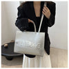 A woman holds a silver tote bag with a leather strap against a white background.