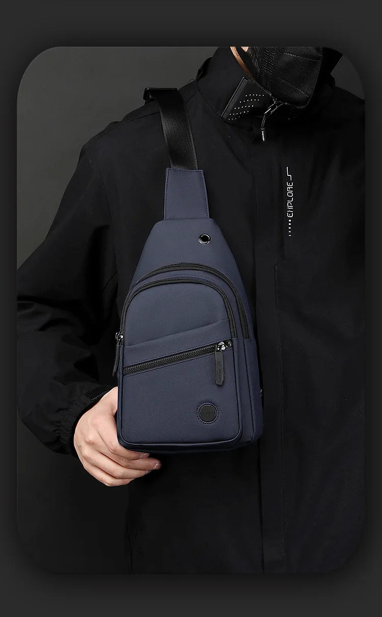 A navy blue lightweight nylon crossbody sling bag is shown attached to a black jacket.