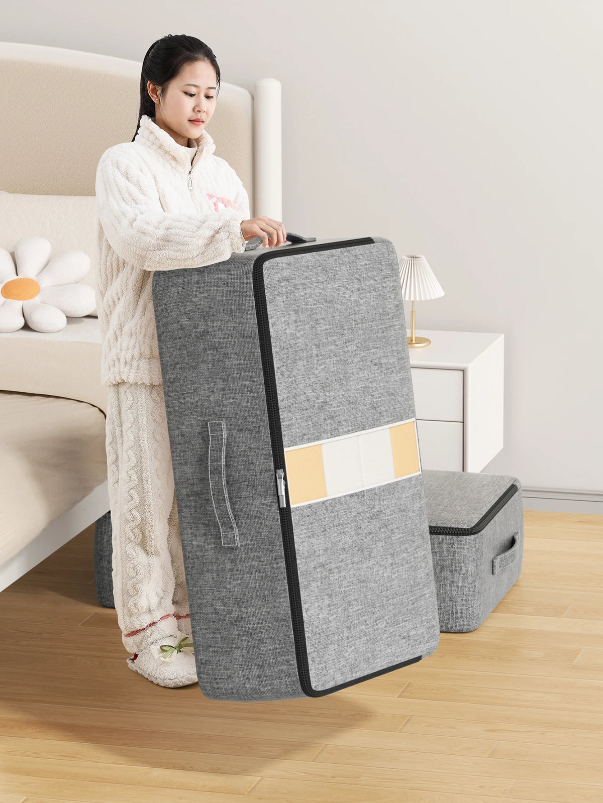 A woman stands next to a gray foldable underbed storage bag in a bedroom setting.