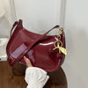 A deep burgundy PU leather shoulder bag with a gold cherry pendant is held by a hand against a white background.