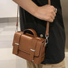 A person holds a tan leather minimalist crossbody bag against a black shirt.