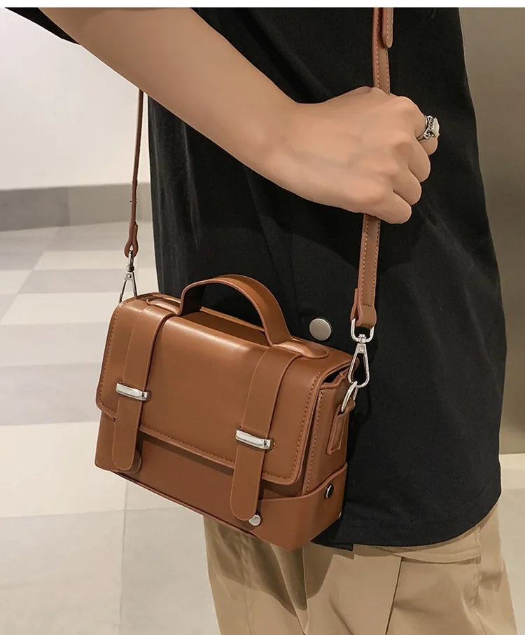 A person holds a tan leather minimalist crossbody bag against a black shirt.