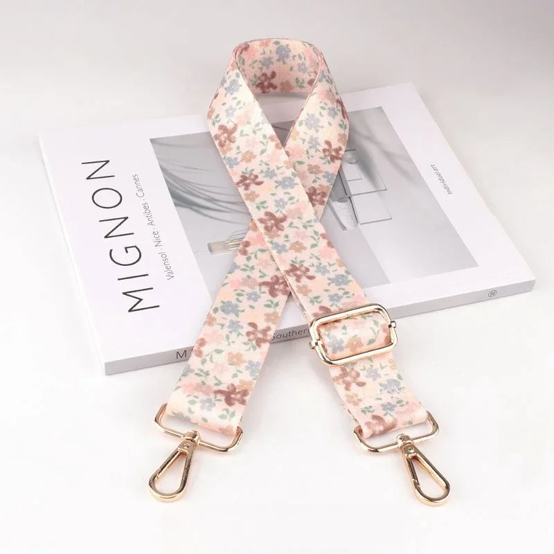 A light pink floral patterned diagonal shoulder strap for bags displayed next to a product box.