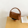 A tan faux suede crossbody bag resting on a light wood block against a white background.