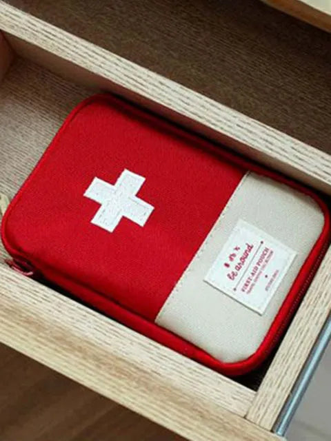 A red compact survival and first aid kit with a white cross on a light background inside a wooden box.